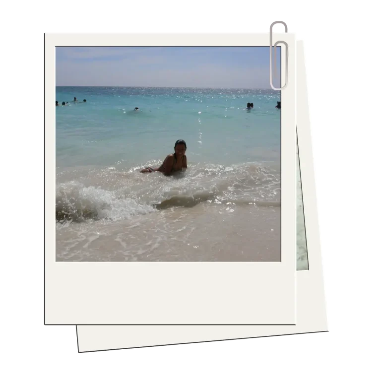 Mujer sonriendo mientras disfruta del mar en una playa paradisíaca de la Riviera Maya, con olas rompiendo suavemente a su alrededor.